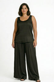 Woman wearing a black sleeveless top and wide-leg pants on a white background