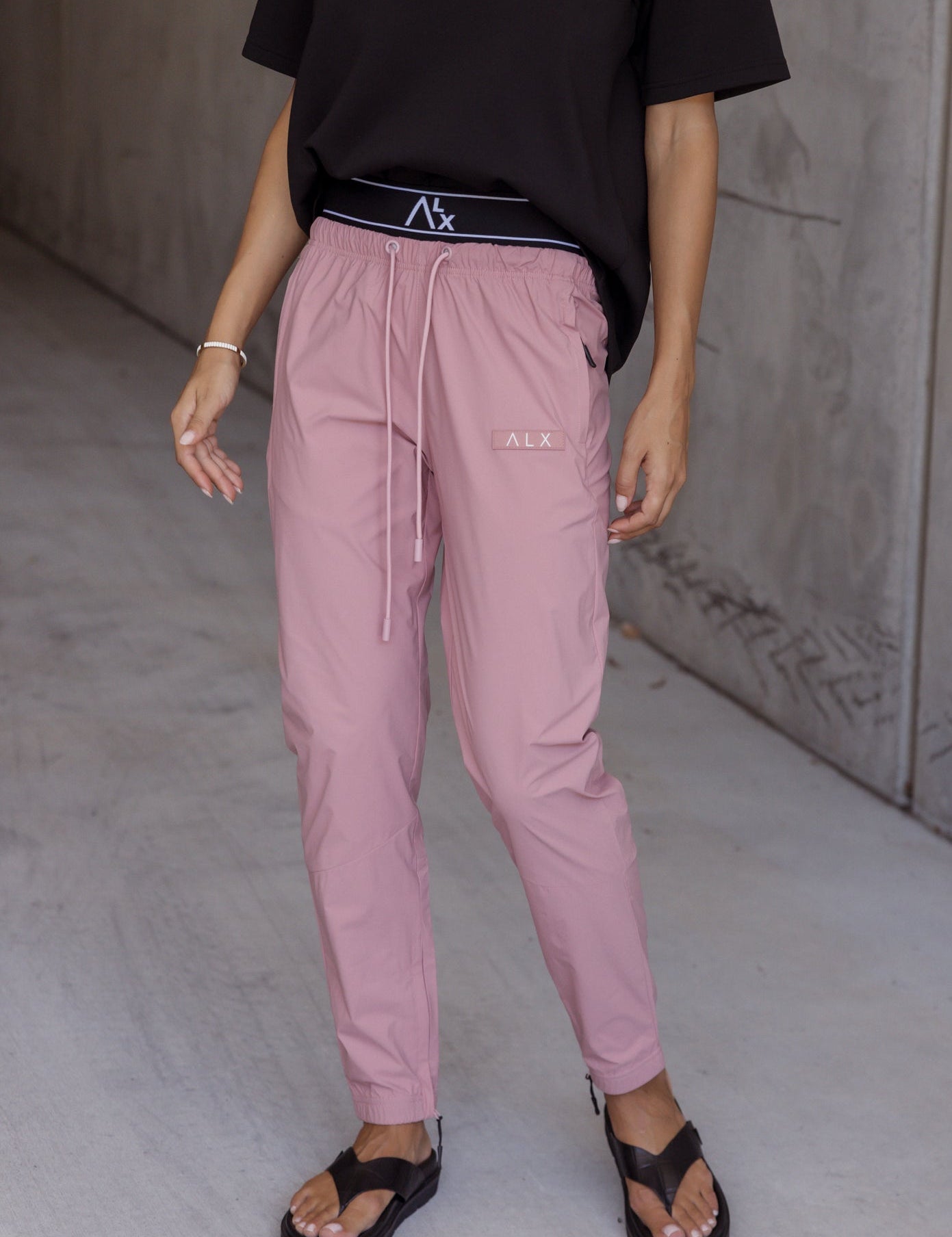 Person wearing pink jogger pants and a black t-shirt with a ALX 
brand logo.